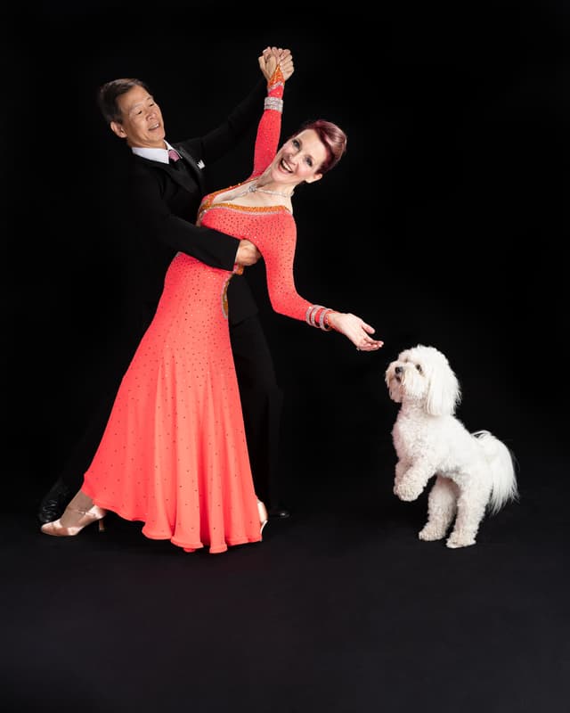 Man and woman posing in an oversway with wite dog standing on hind legs