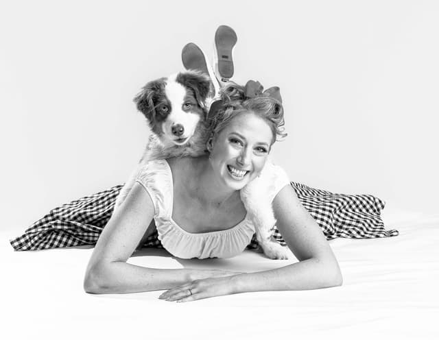 Woman posing on floor facing camera with dog on her back looking at camera over her shoulder