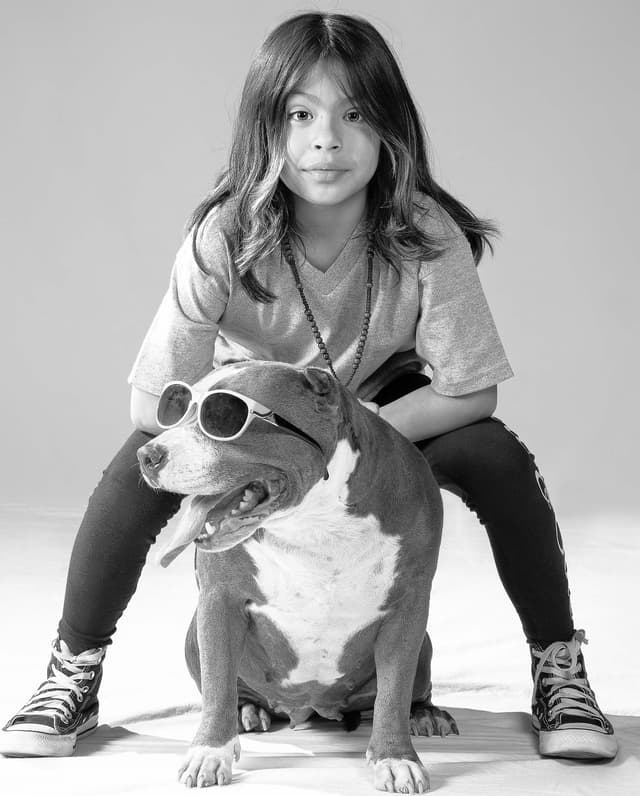 Girl in hip hop pose behind dog wearing sunglasses